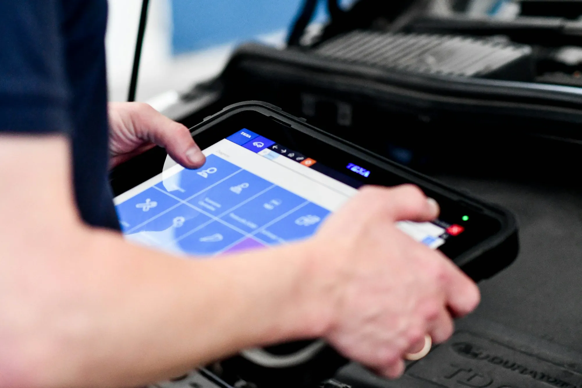 Technician holding a diagnostic tablet near a car